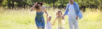 A host family and two young children running through a sunlit meadow on a summer day